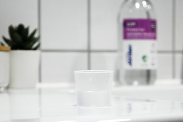 mouthwash cup on bathroom counter with mouth wash bottle in the background